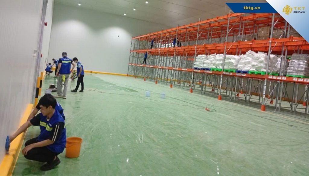 Công nhân làm sạch sàn xưởng cạnh dãy kệ hàng trong nhà máy